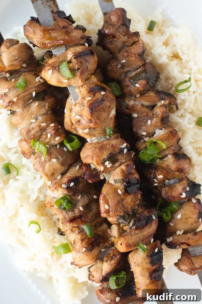 Gluten-Free Teriyaki Marinade Recipe for Stir-Fries & Grilling 3 Top down shot of grilled chicken pieces on metal skewers over white rice with sesame seeds and chopped green onion on top.