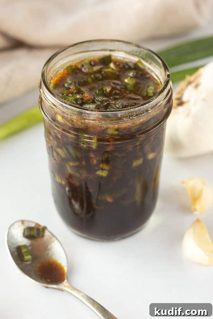 Gluten-Free Teriyaki Marinade Recipe for Stir-Fries & Grilling 5 An angled shot of a mason jar with a brown marinade with chopped green onions in it with a small dirty spoon to the left and fresh green onions and cloves of garlic surrounding it.