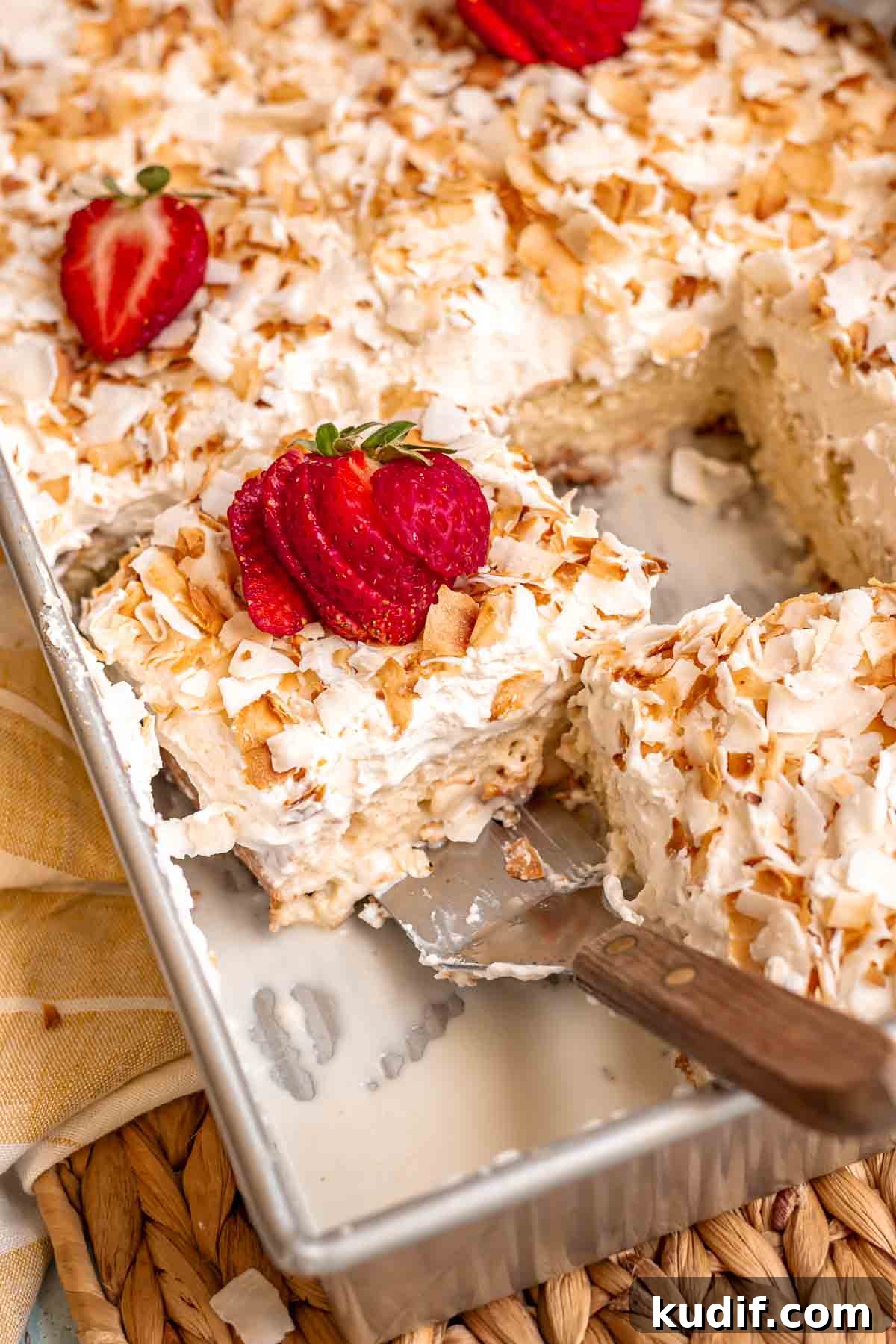 Coconut Tres Leches Cake Recipe — Moist Latin-Style Dessert 2 A spatula removes a soaked piece of coconut tres leches cake from a pan.