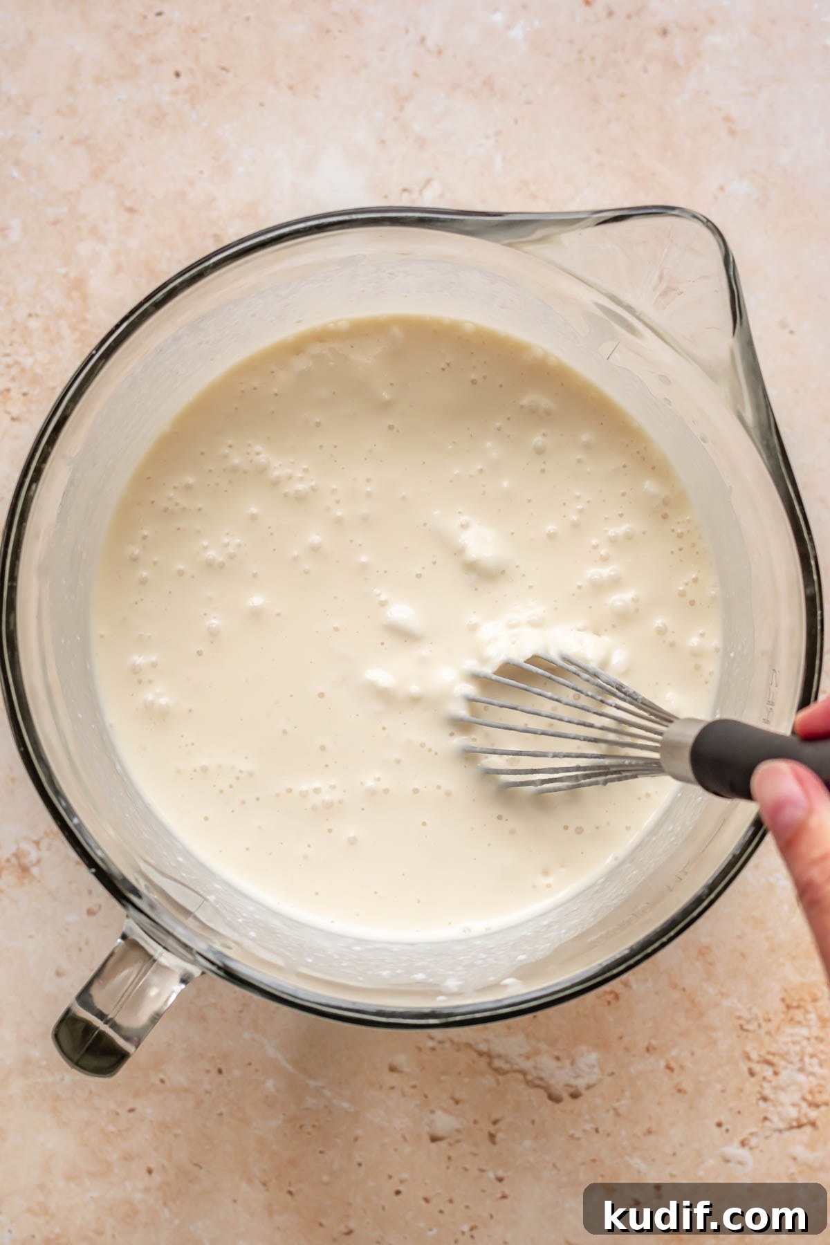 Coconut Tres Leches Cake Recipe — Moist Latin-Style Dessert 12 A hand whisks a mixture of milks in a large measuring cup.