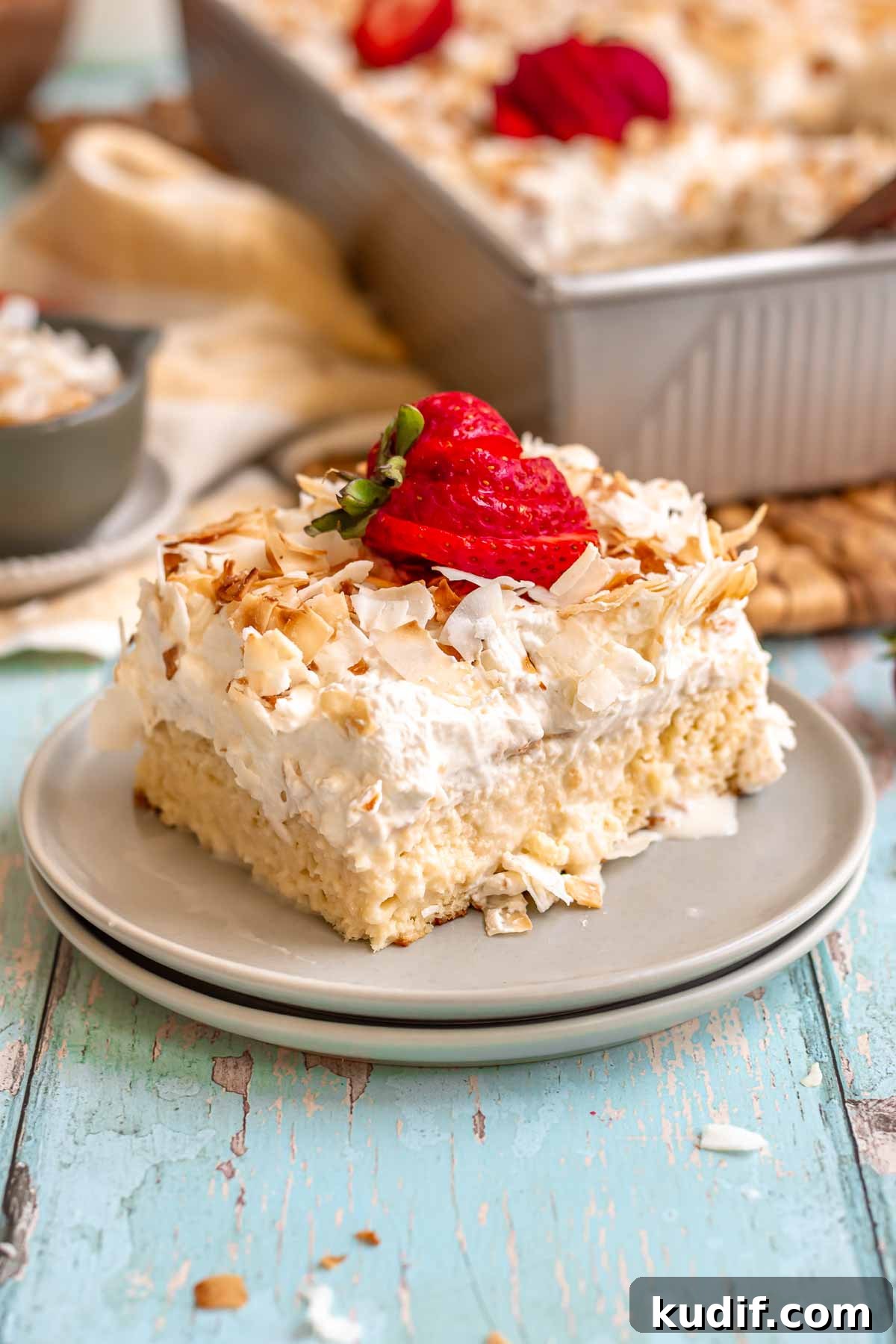 Coconut Tres Leches Cake Recipe — Moist Latin-Style Dessert 17 A slice of coconut tres leches cake on a plate with strawberries on top.