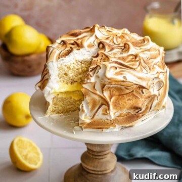 Lemon meringue cake on a stand with a slice removed.