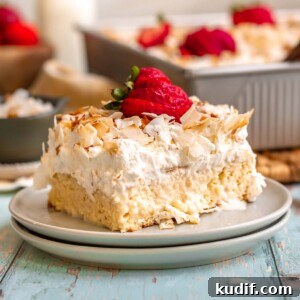 Coconut Tres Leches Cake Recipe — Moist Latin-Style Dessert 23 A slice of coconut tres leches cake on a plate with sliced strawberries on top.