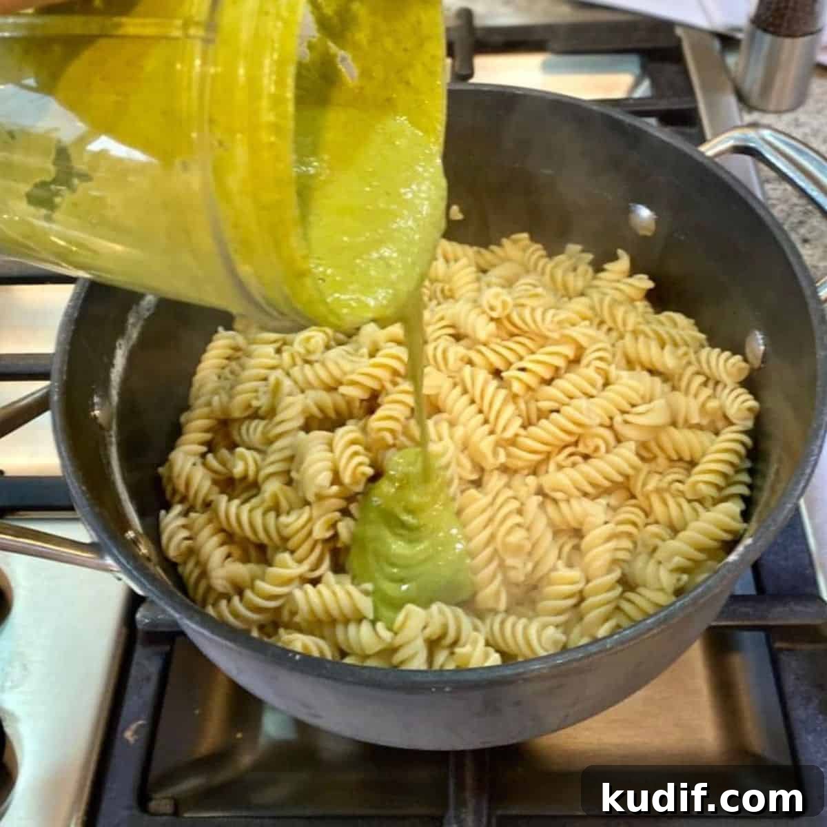 I am adding pesto sauce to the cooked noodles in a pan.