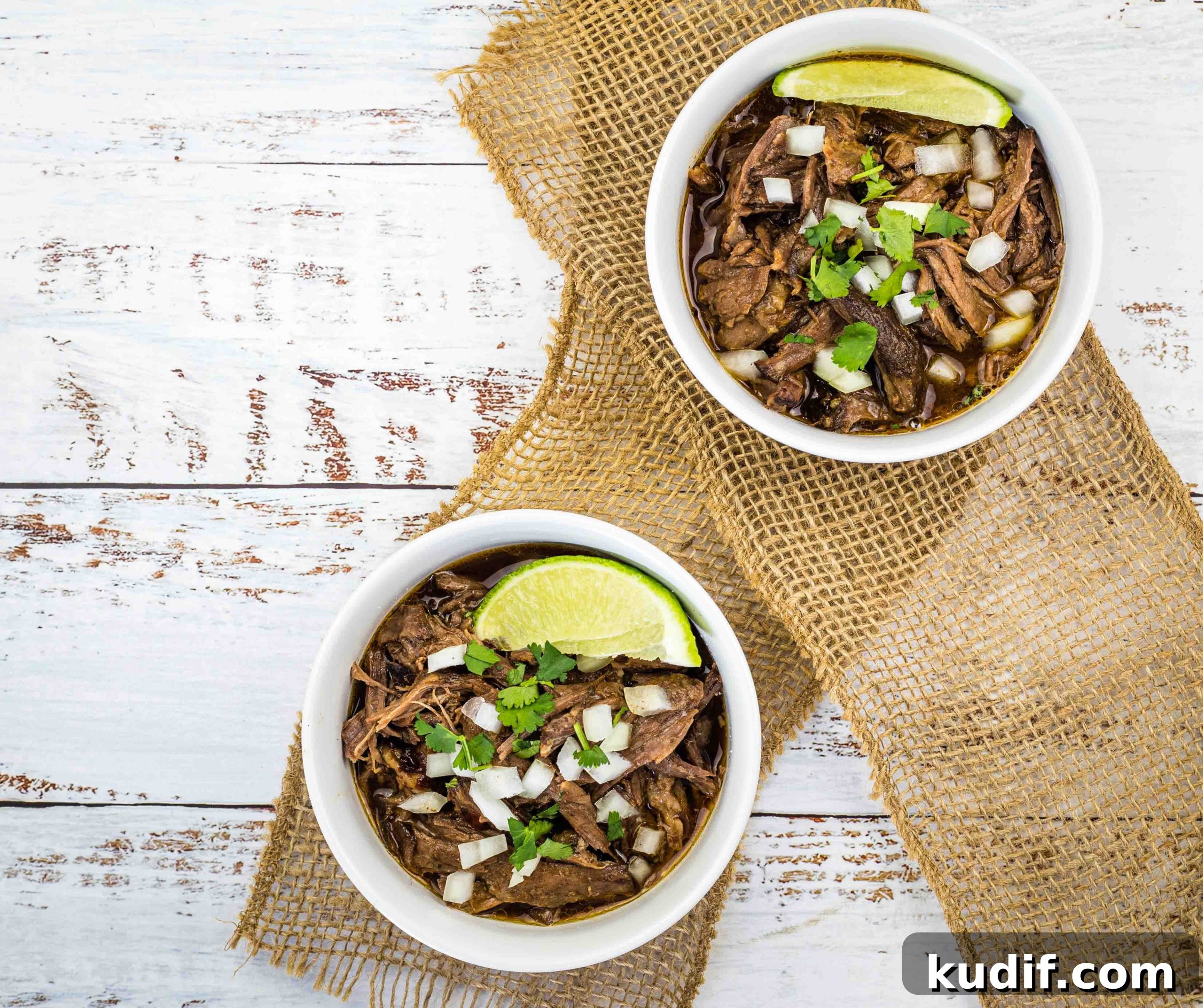 31 Delicious Recipes That Deliver Big Flavor with Little Effort 25 Two white bowls filled with slow cooker birria garnished with fresh lime wedges.