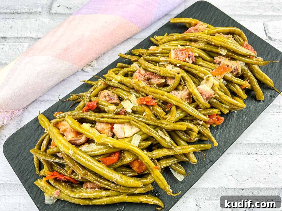 31 Delicious Recipes That Deliver Big Flavor with Little Effort 27 A plate of cooked Southern Green Beans with sliced sausages and tomato pieces on a white dish, placed near a sunflower.