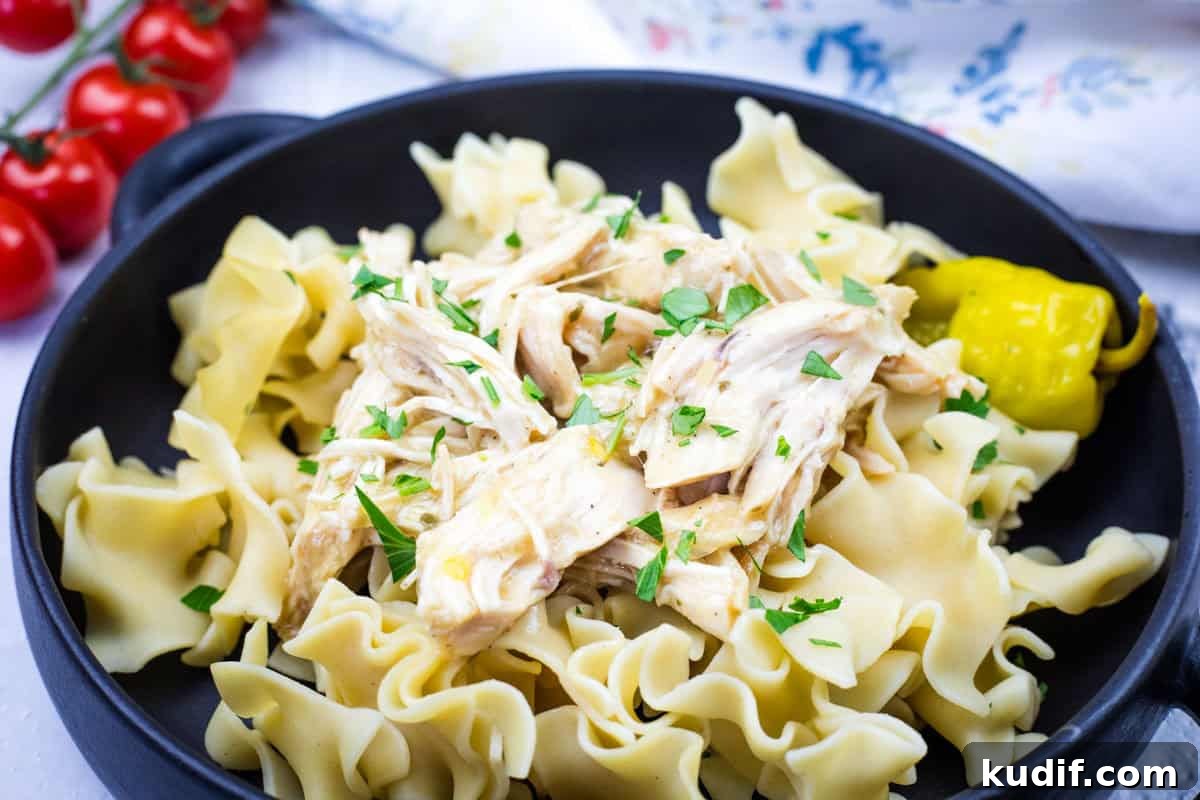 31 Delicious Recipes That Deliver Big Flavor with Little Effort 5 A black bowl containing egg noodles topped with Slow Cooker Mississippi Chicken and garnished with parsley, accompanied by a pickled pepper.