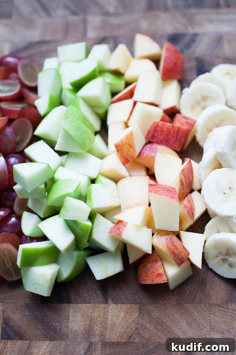 Creamy Holiday Fruit Salad with Cinnamon and Citrus 3 Wooden cutting board with chopped fruit.