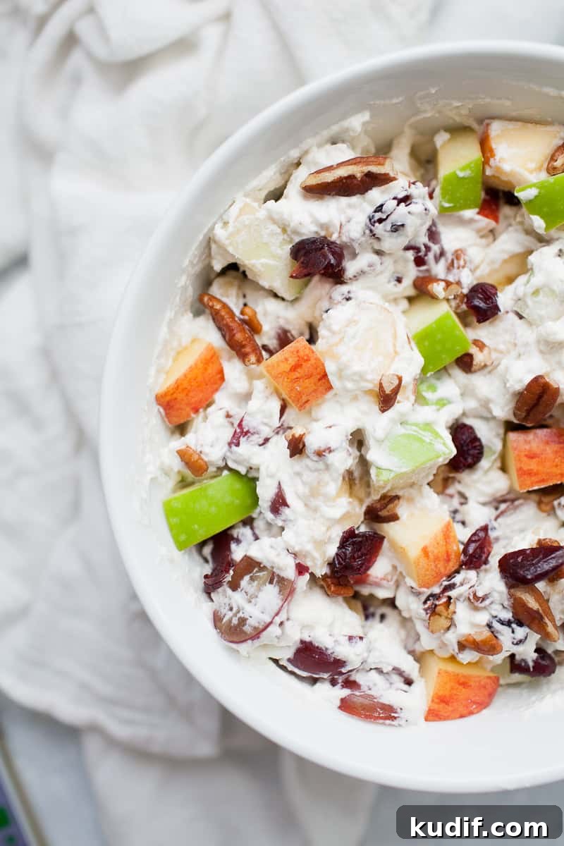 Creamy Holiday Fruit Salad with Cinnamon and Citrus 5 White bowl with creamy whipped cream topped fruit salad with red and green apples, grapes, bananas, cranberries and pecans.
