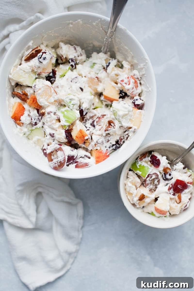 Creamy Holiday Fruit Salad with Cinnamon and Citrus 7 White bowls with creamy whipped cream topped fruit salad with red and green apples, grapes, bananas, cranberries and pecans.