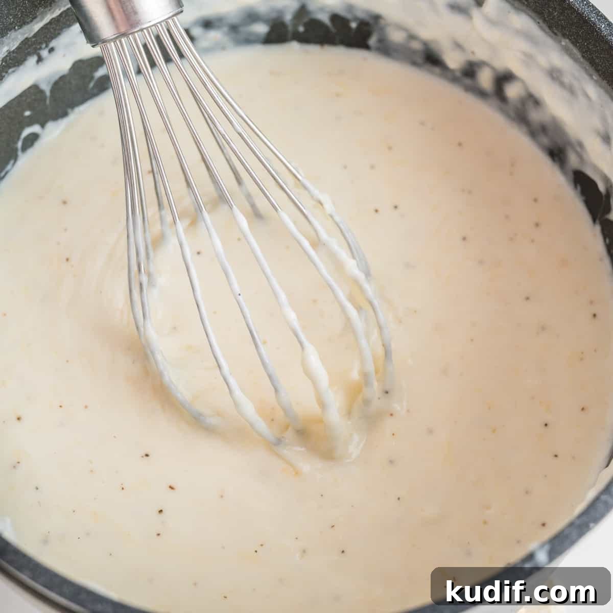 Creamy Homemade Alfredo Sauce Using Milk — Simple Recipe 10 Close up of alfredo sauce in a pot with a whisk.