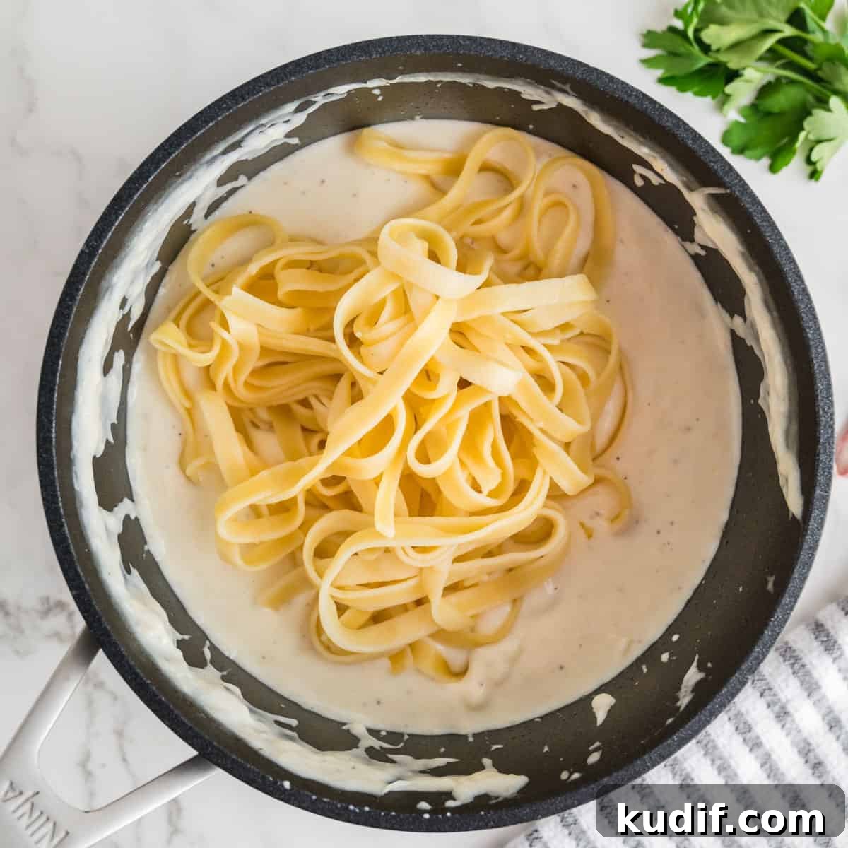 Creamy Homemade Alfredo Sauce Using Milk — Simple Recipe 11 Noodles in an alfredo sauce in a black pot.
