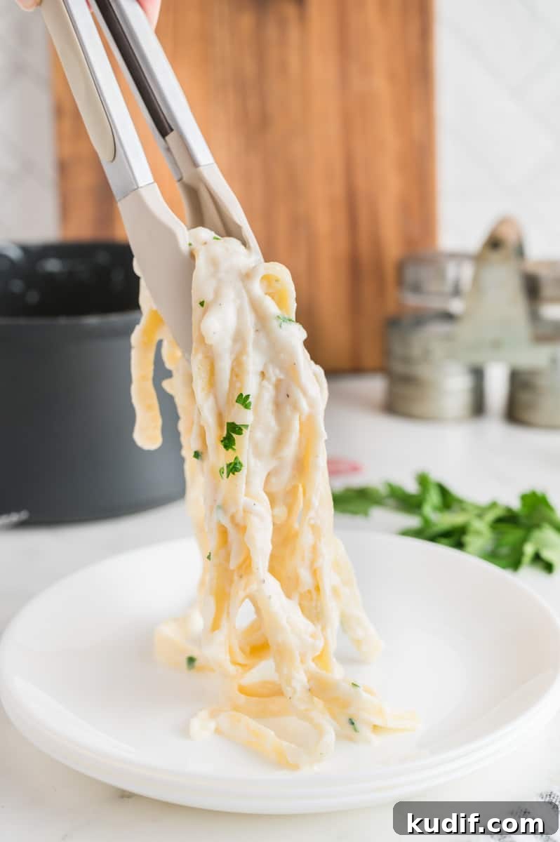 Creamy Homemade Alfredo Sauce Using Milk — Simple Recipe 13 Tongs holding up fettuccine alfredo over a plate.