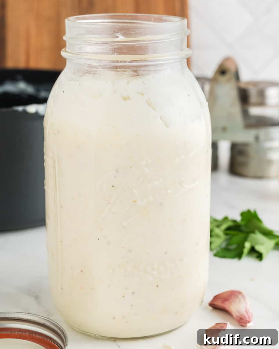 Creamy Homemade Alfredo Sauce Using Milk — Simple Recipe 14 Alfredo sauce in a jar with basil and garlic around.