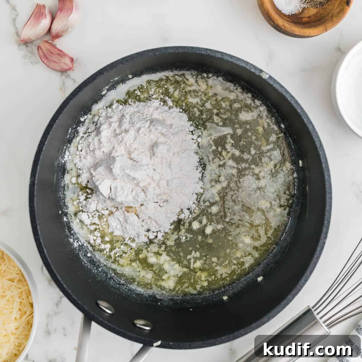 Creamy Homemade Alfredo Sauce Using Milk — Simple Recipe 5 Flour added to butter and garlic in a black pan.