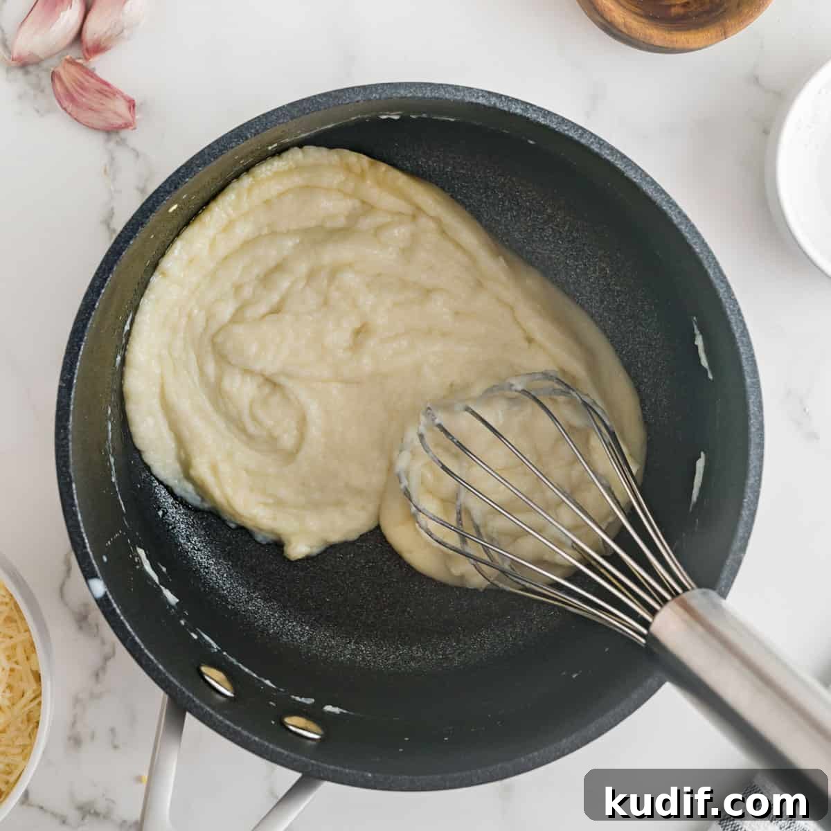 Creamy Homemade Alfredo Sauce Using Milk — Simple Recipe 7 milk added to the roux in a black pan with a whisk.