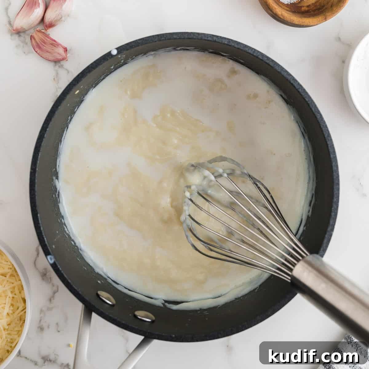 Creamy Homemade Alfredo Sauce Using Milk — Simple Recipe 8 Black pot filled with sauce, with whisk.