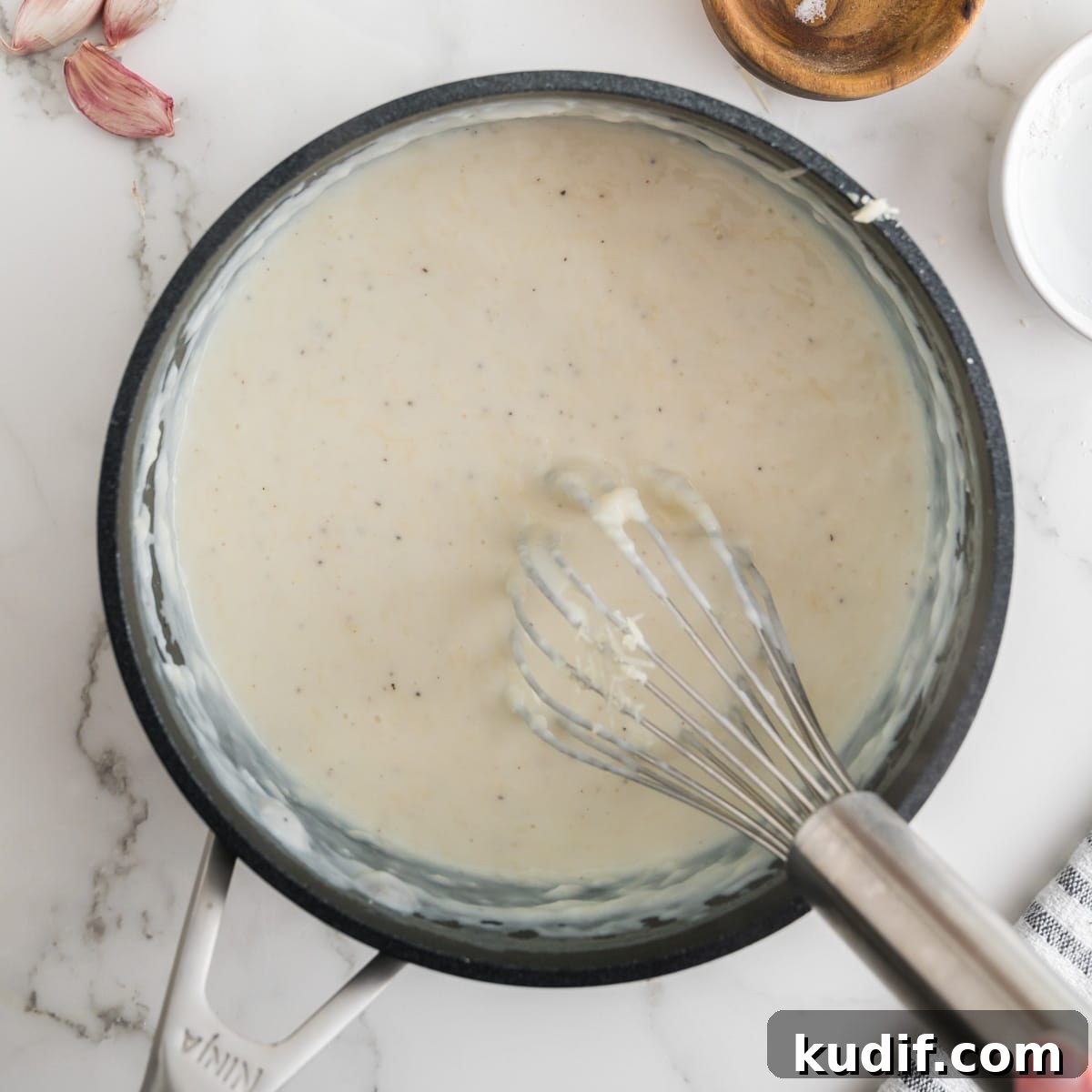 Creamy Homemade Alfredo Sauce Using Milk — Simple Recipe 9 Alfredo sauce in a black pot with a whisk.