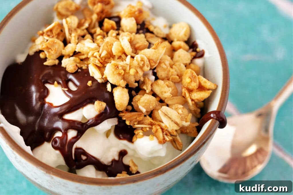 Classic Old-Fashioned Hot Fudge Sauce Recipe 10 A close-up image looking into a pale blue bowl with vanilla yogurt, hot fudge sauce, and granola in it.