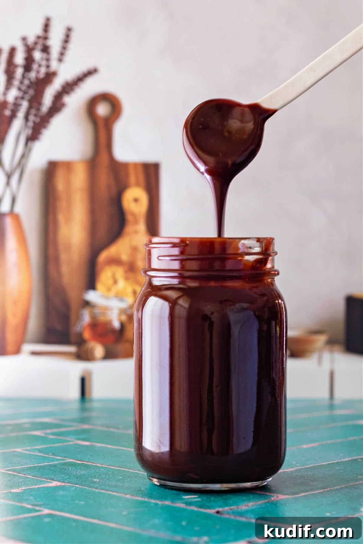Classic Old-Fashioned Hot Fudge Sauce Recipe 7 A white spoon with hot fudge sauce drizzling off it and back into the jar below.
