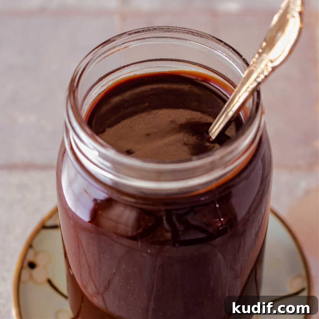 Classic Old-Fashioned Hot Fudge Sauce Recipe 11 A square image looking down into a jar of fudge sauce with a spoon in it.