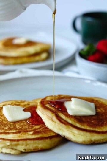 Syrup pouring over pancakes on gray plate.