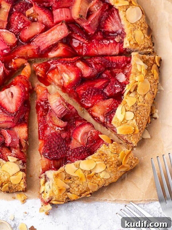 Sliced strawberry rhubarb galette with almond crust on parchment paper.