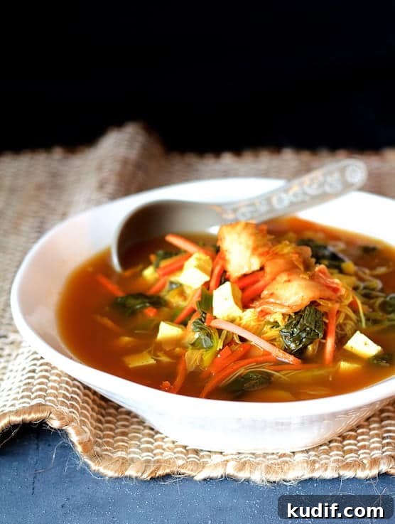 Comforting Asian Vegetable and Tofu Soup Recipe 2 Photo of Asian Vegetable Soup with Tofu Kimchi and Rice Noodles in white bowl on brown burlap and blue background.