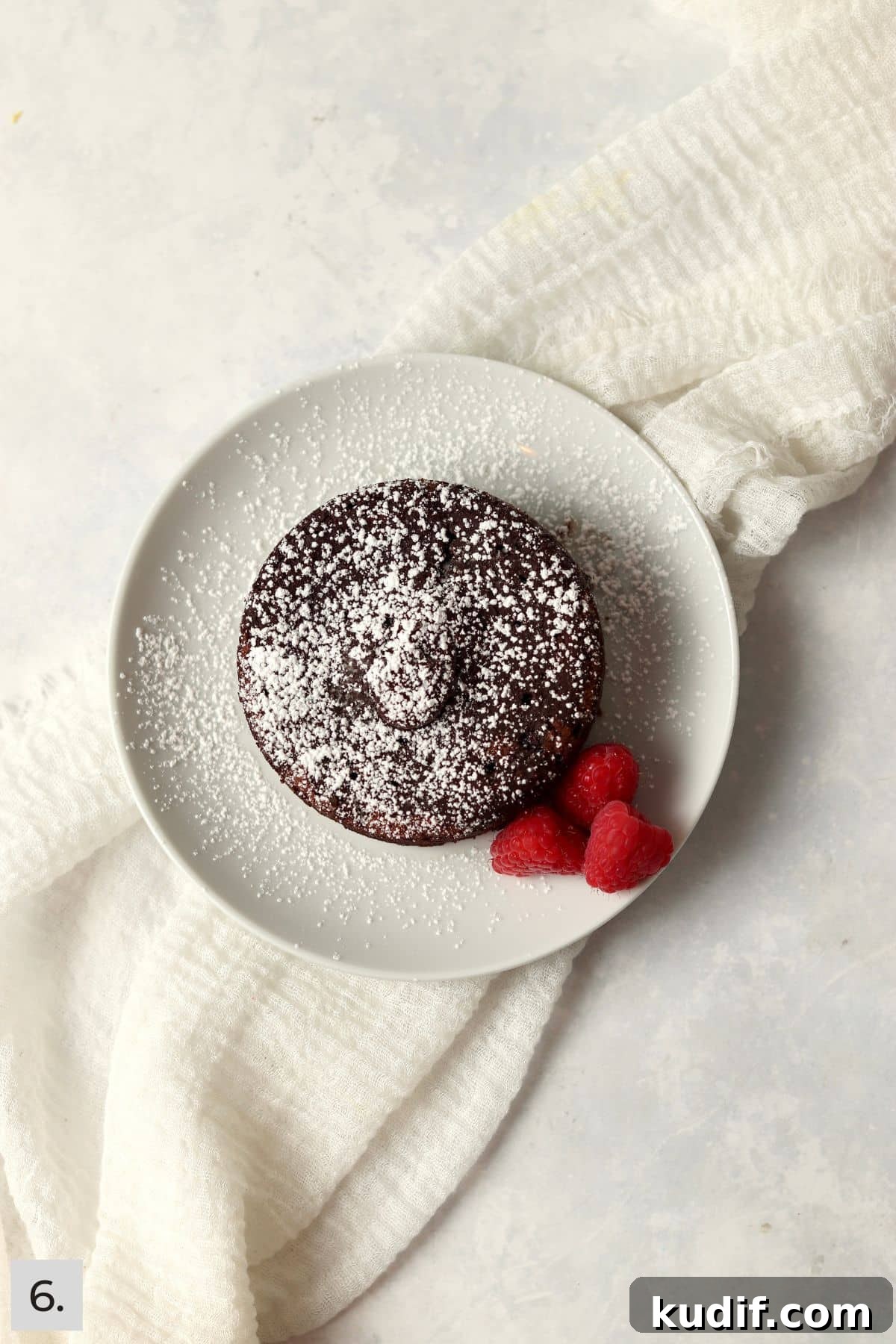 Individual chocolate lava cake on a plate dusted with powdered sugar and fresh raspberries.