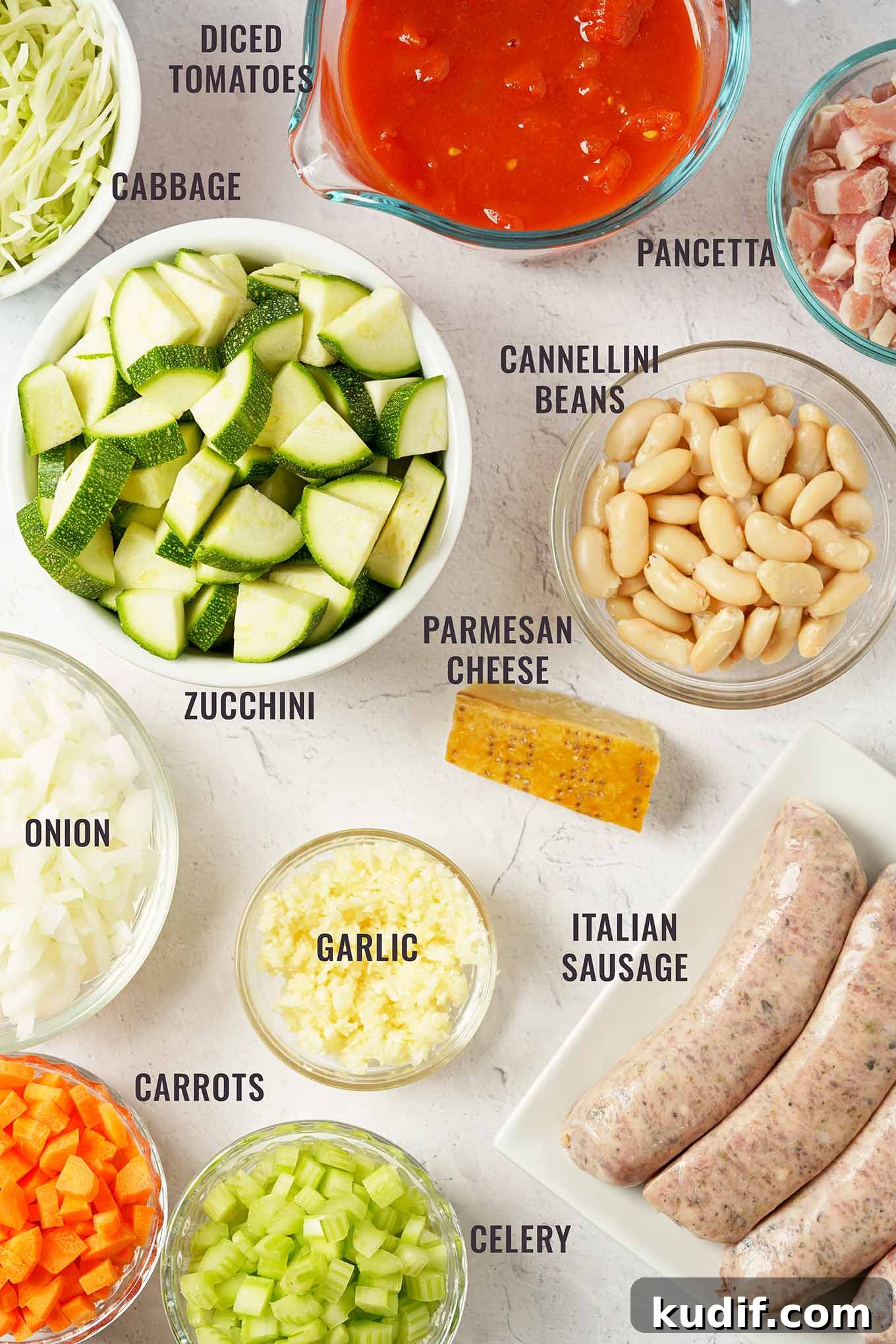 Sausage Minestrone Soup with Vegetables and Beans 3 A labeled overhead view of ingredients for minestrone soup including Italian sausage, zucchini, cannellini beans, pancetta, carrots, celery, onion, and more.