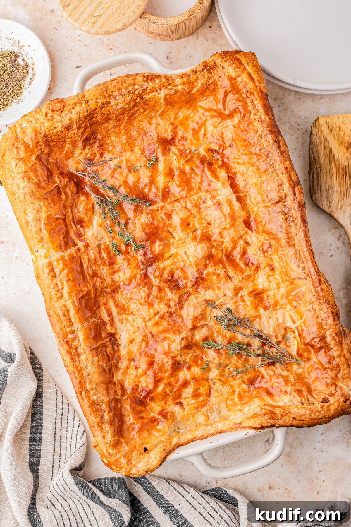 Comforting Chicken Pot Pie Casserole Recipe for Weeknights 3 Golden-brown rectangular pie with a flaky crust, garnished with sprigs of herbs, in a white baking dish on a light countertop.