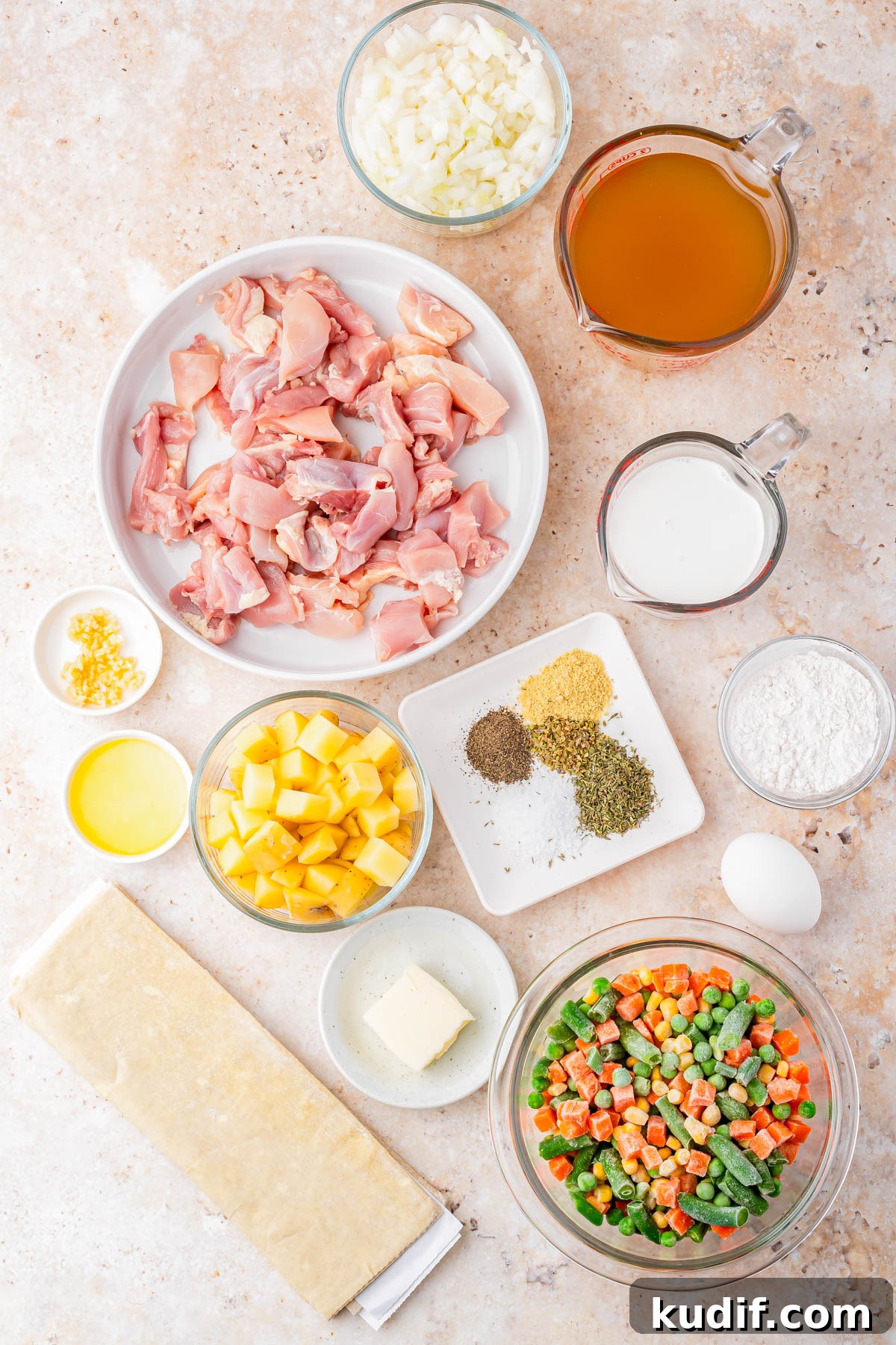 Comforting Chicken Pot Pie Casserole Recipe for Weeknights 5 Top-down view of prepped ingredients for chicken pot pie, including chopped chicken, vegetables, broth, milk, seasonings, butter, egg, flour, and a sheet of pastry on a light surface.