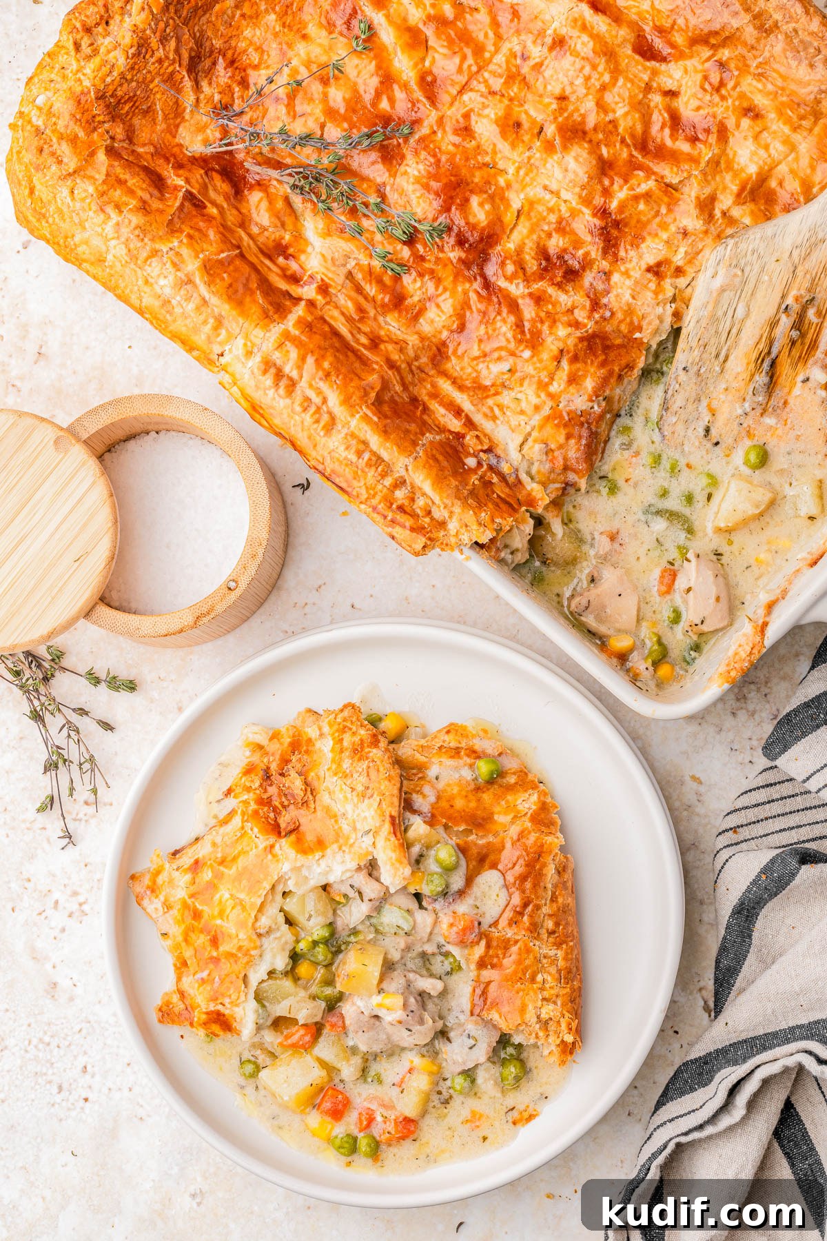 Comforting Chicken Pot Pie Casserole Recipe for Weeknights 6 A serving of chicken pot pie with golden, flaky crust and mixed vegetables on a white plate, beside a baking dish containing the remaining pie.