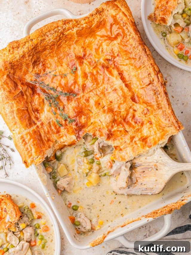 Comforting Chicken Pot Pie Casserole Recipe for Weeknights 7 Golden-brown puff pastry-topped chicken pot pie in a baking dish, partially served with filling of chicken and mixed vegetables, surrounded by two plated servings.