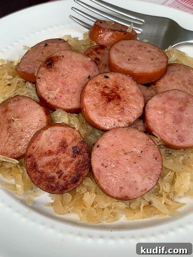 Kielbasa and Sauerkraut Recipes: Classic Polish Sausage Dishes 5 Browned Kielbasa on sauerkraut with fork on white plate.