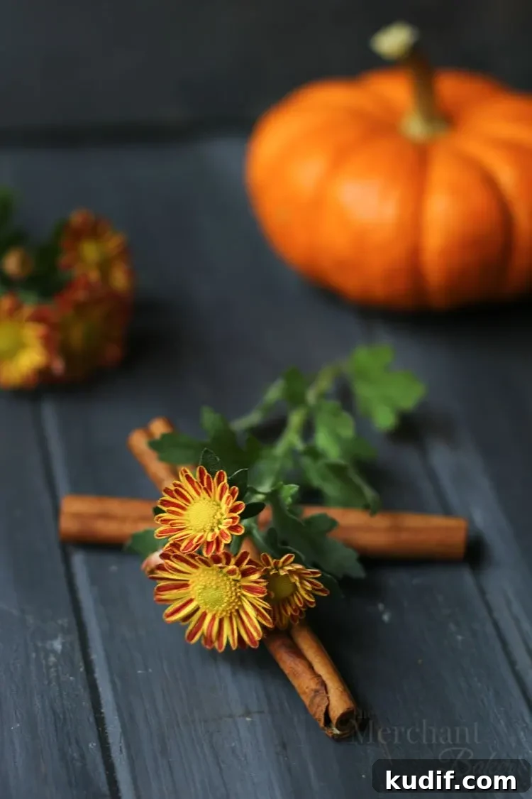 Pumpkin Scones Recipe: Flaky Spiced Scones for Fall Baking 4 Cinnamon and flowers to be displayed with the best pumpkin scones displayed on a raw wood slab by themerchantbaker.com