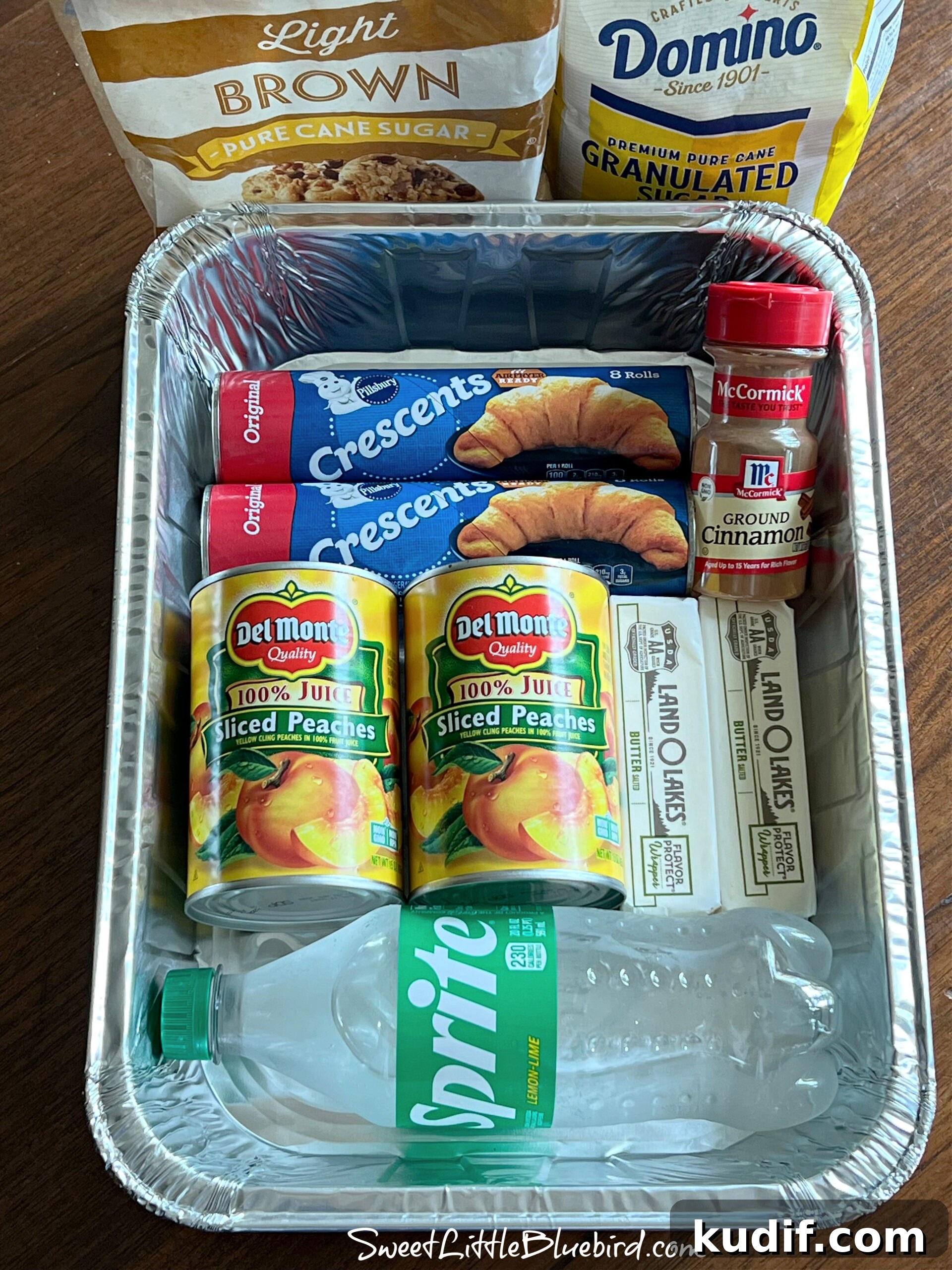 Crescent Roll Peach Dumplings with Warm Cinnamon Sauce 3 Ingredients arranged in a disposable 9x13 pan: canned peaches, crescent rolls, butter, cinnamon, and a bottle of Sprite with sugar bags nearby.