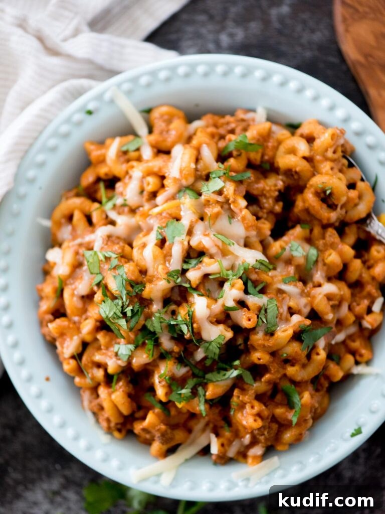 Cheesy Taco & Cream Cheese Pasta Recipe for Weeknight Dinners 2 one pot cheesy taco pasta in a blue bowl topped with cheese and cilantro