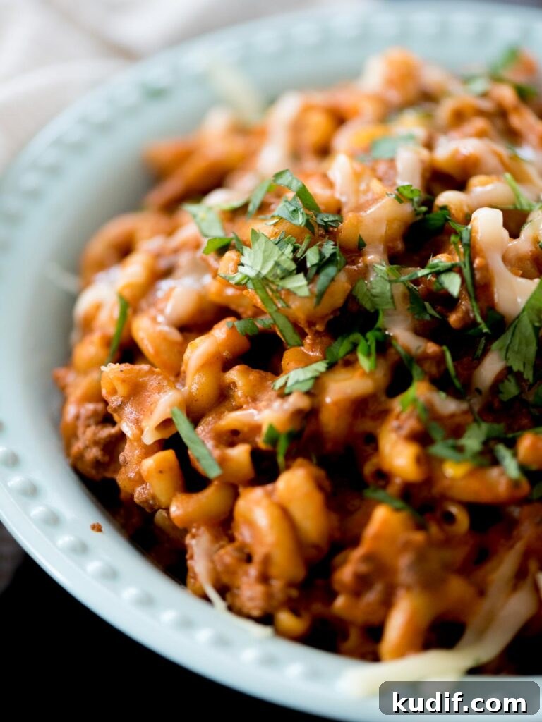 Cheesy Taco & Cream Cheese Pasta Recipe for Weeknight Dinners 9 one pot cheesy taco pasta in a blue bowl topped with cheese and cilantro