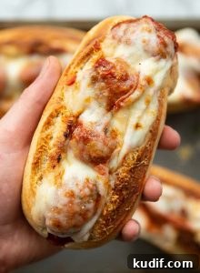 hand holding meatball sub above tray of subs fresh out the oven