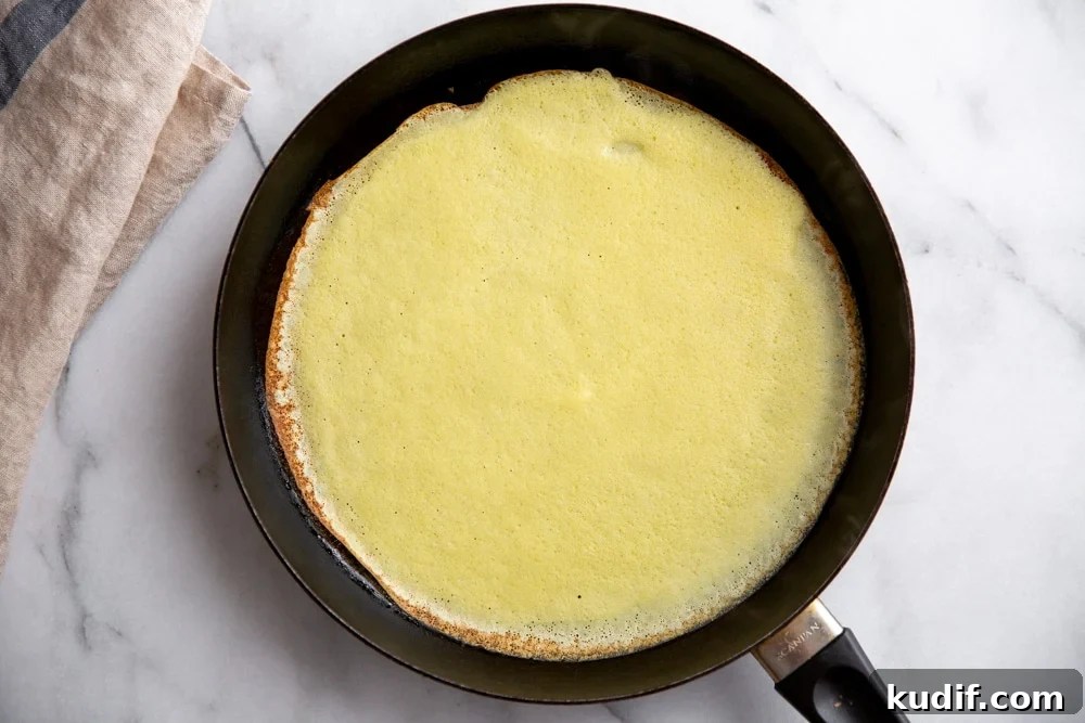 Process shot showing a crepe cooking in a non-stick skillet.