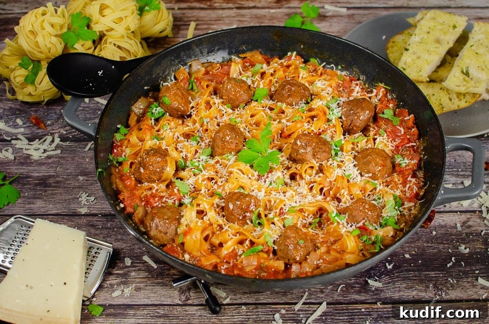 Spicy One-Pot Meatball Pasta Recipe for Quick Dinners 2 One-Pot Spicy Meatball Pasta served in a cast iron pan with sprinkled chopped parsley on top for garnish, with garlic bread served on the side on a grey Parmesan cheese with a silver grater, black spoon to serve the food and dry balls of tagliatelle in the background of the picture