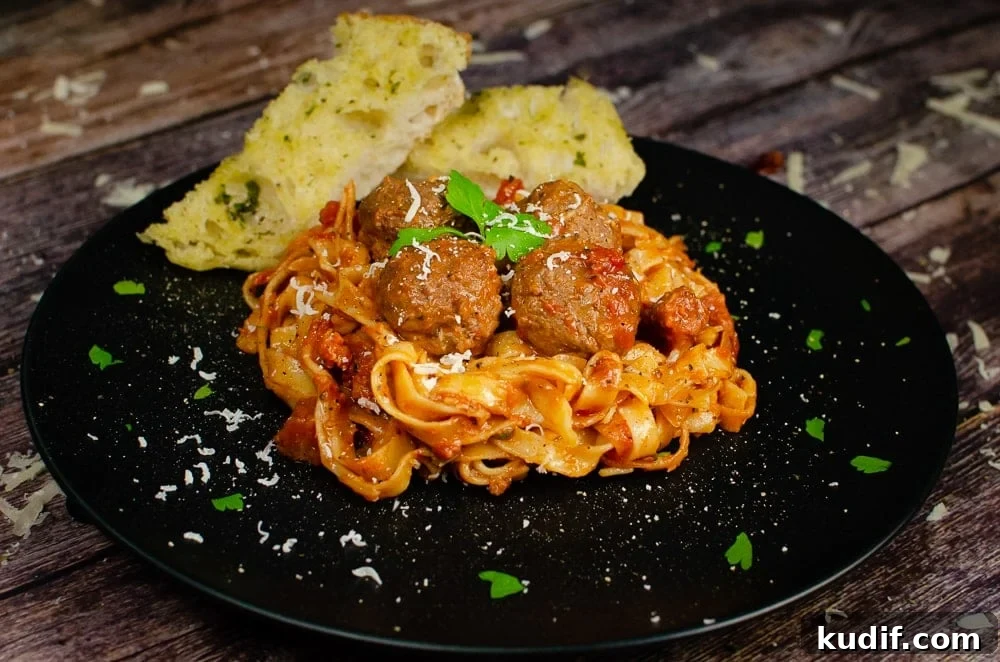 Spicy One-Pot Meatball Pasta Recipe for Quick Dinners 4 Spicy Meatball Pasta served on a black plate with garlic bread on the side with a garnish of chopped parsley and grated parmesan over the top of the food