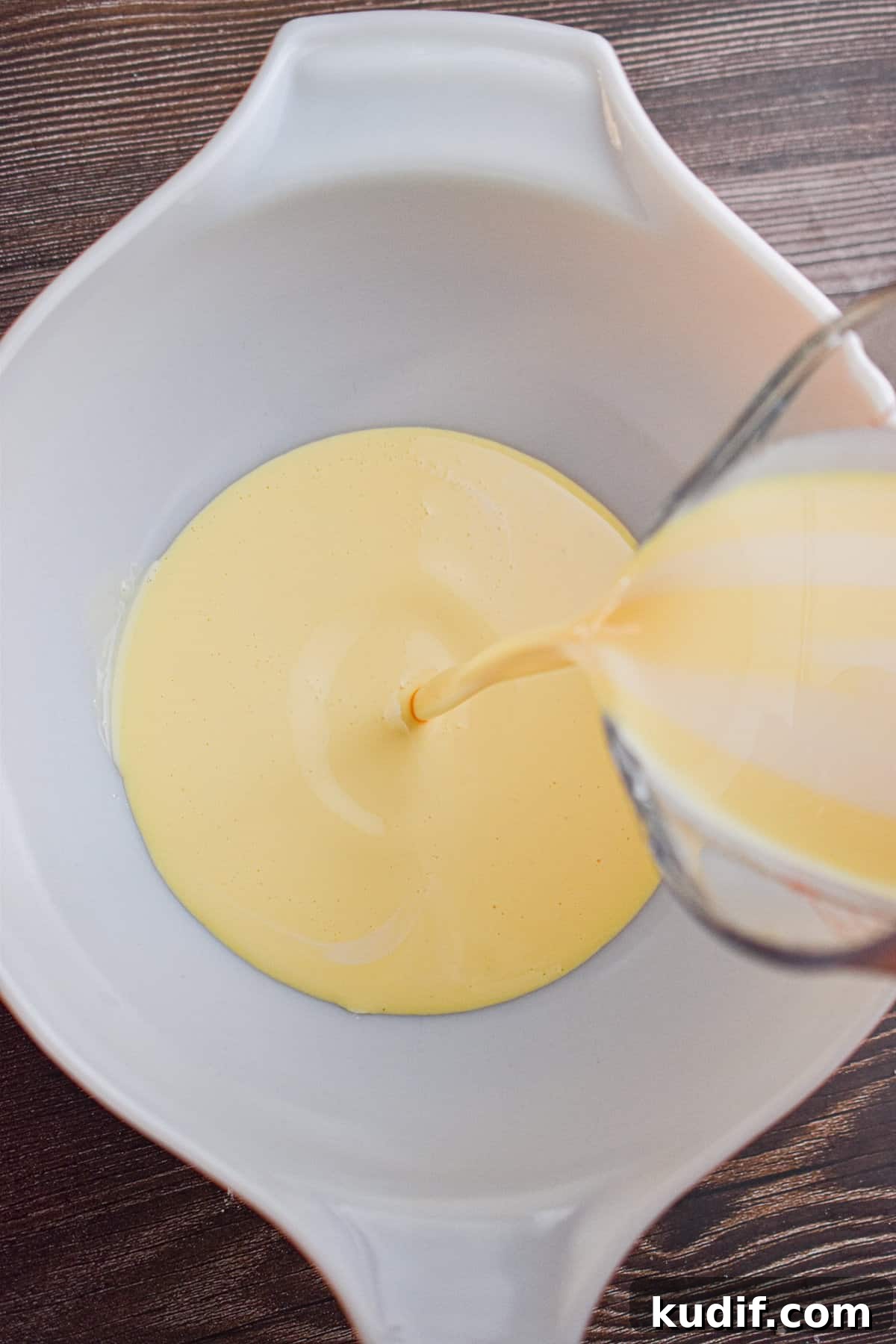 The eggnog is being poured into a large mixing bowl.