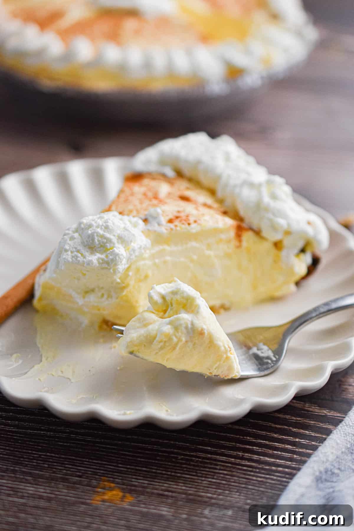 A piece of the no-bake eggnog pie is on a plate with a fork holding a piece of that pie.