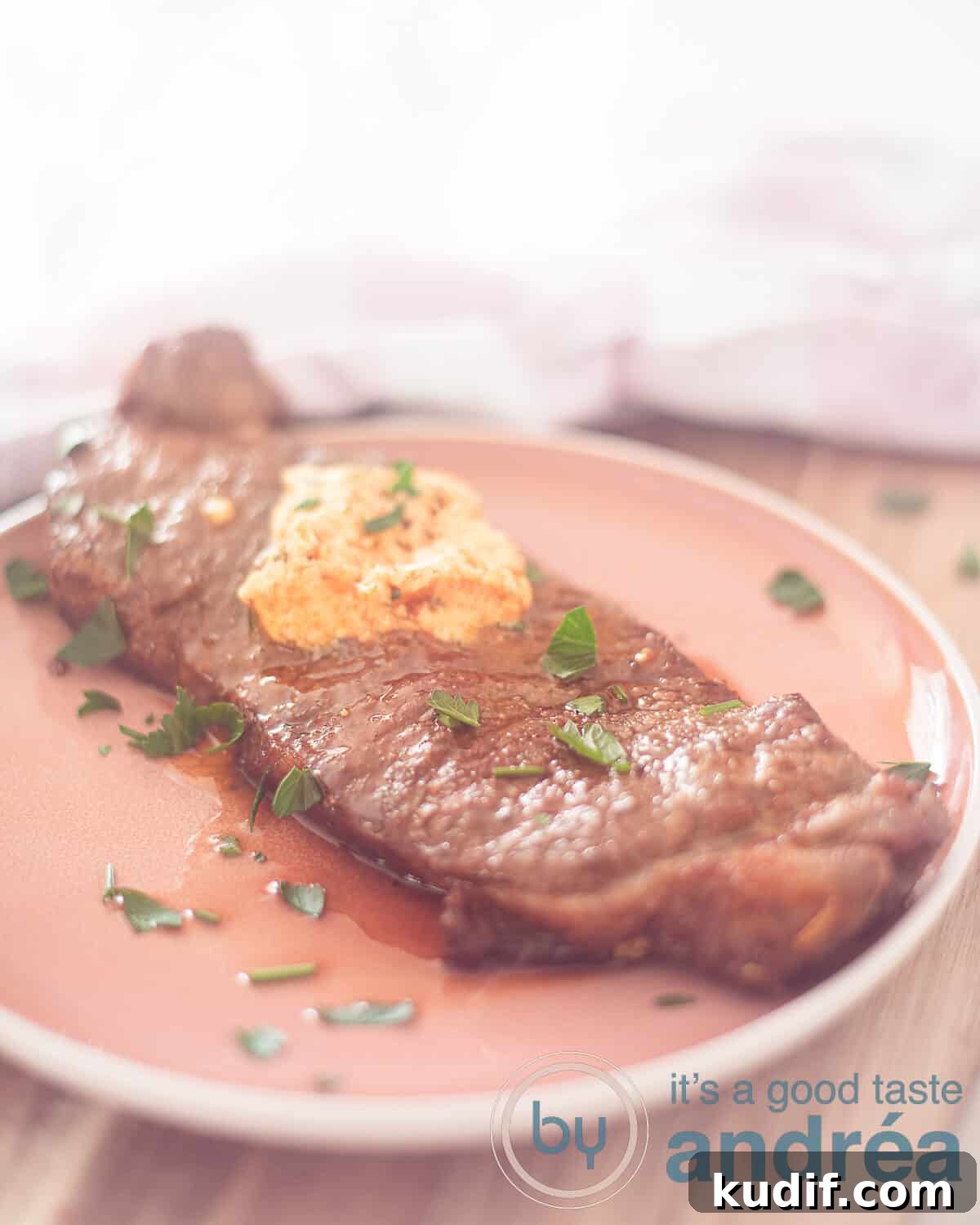 Crispy Air Fryer Sirloin Steak in 15 Minutes 2 A pink plate on a wooden shelf with a pink and white checkered tea towel behind it. On the plate sirloin steak with herb butter and parsley