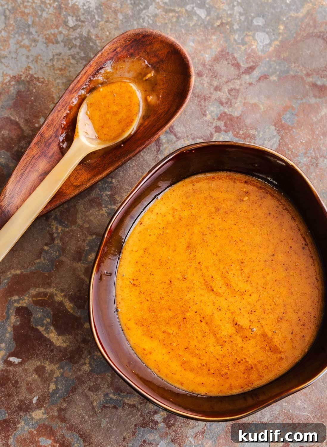 Asian Almond Butter Dipping Sauce (No-Cook) 2 A brown bowl of creamy golden brown Asian dipping sauce and a spoon on the side.