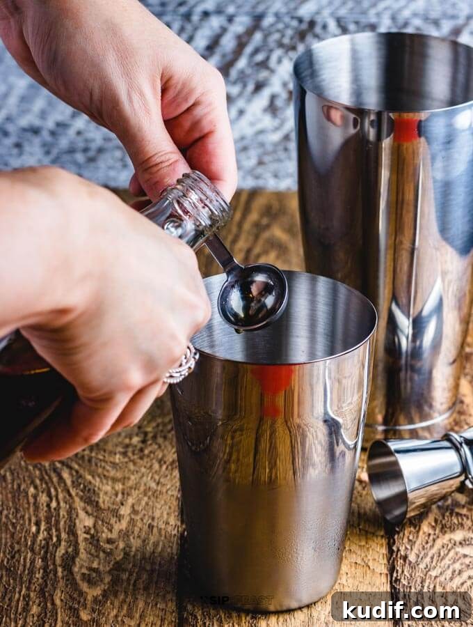 Apple Cider Cocktail - sipandfeast.com #cocktails #bourbon #drinkrecipes Hands measuring a teaspoon of maple syrup and pouring into a cocktail shaker.