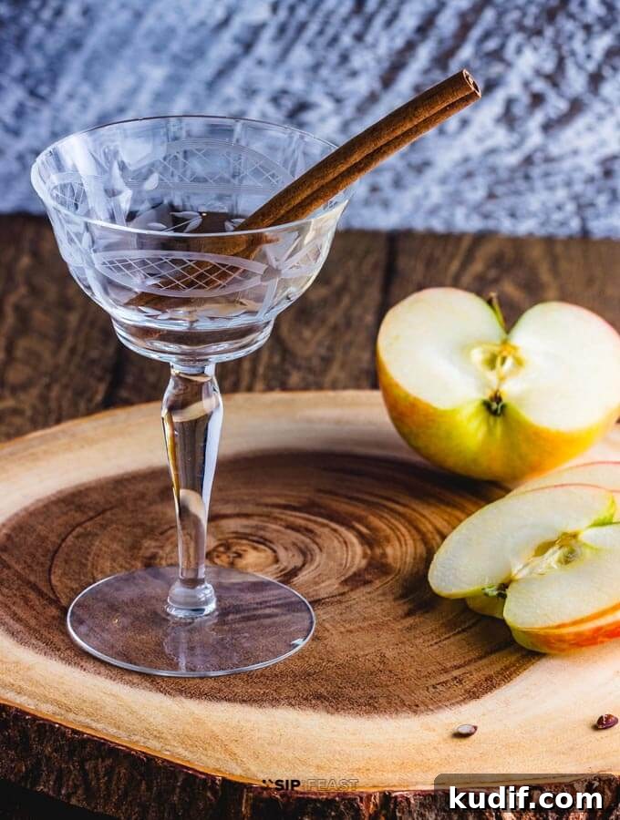 Apple Cider Cocktail - sipandfeast.com #cocktails #bourbon #drinkrecipes Cocktail glass with cinnamon stick, and sliced apples on a cutting board.