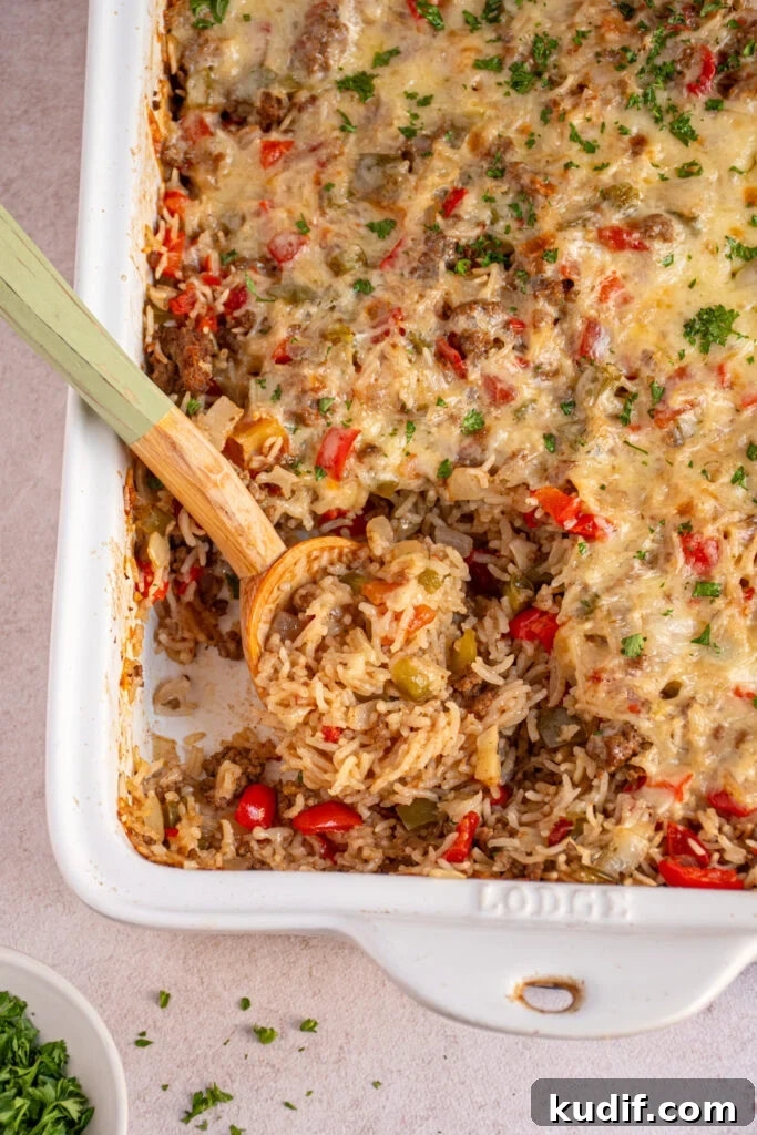 Cheesy Stuffed Pepper Casserole Bake Recipe 9 Stuffed Pepper Casserole in a white baking dish with a wooden spoon that has scooped some out showing cooked rice, ground beef, and bell peppers.